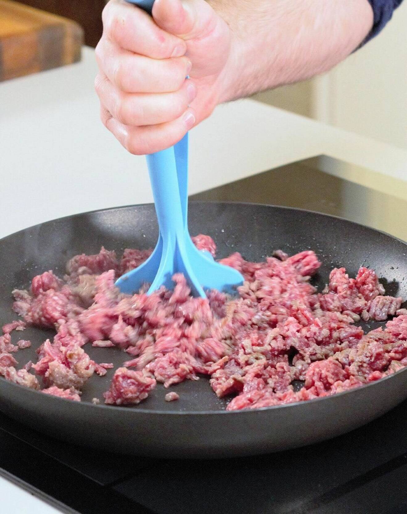 Person använder en köttfärshackare för att få en klumpfri köttfärs i stekpanna.
