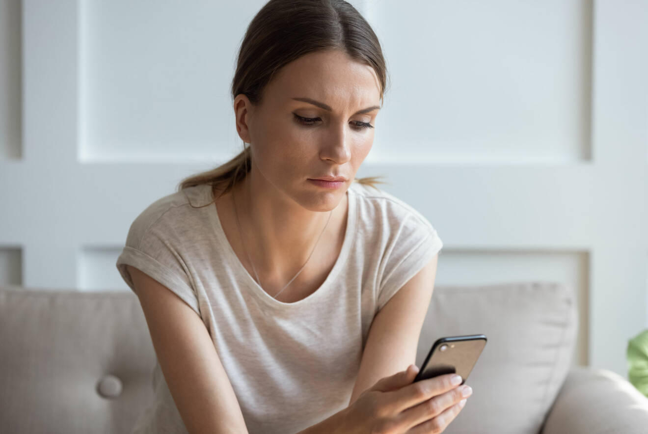 En kvinna sitter med sin mobiltelefon och scrollar.