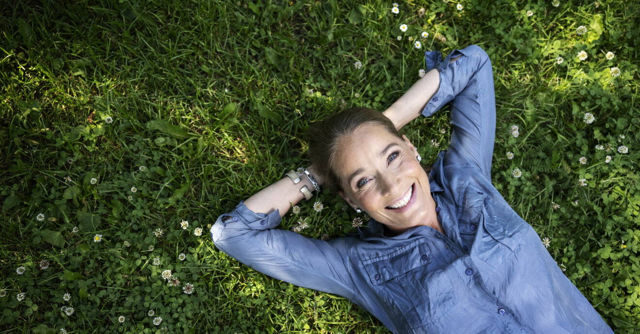 Agneta Sjödin ligger i gräset och tittar leende in i kameran