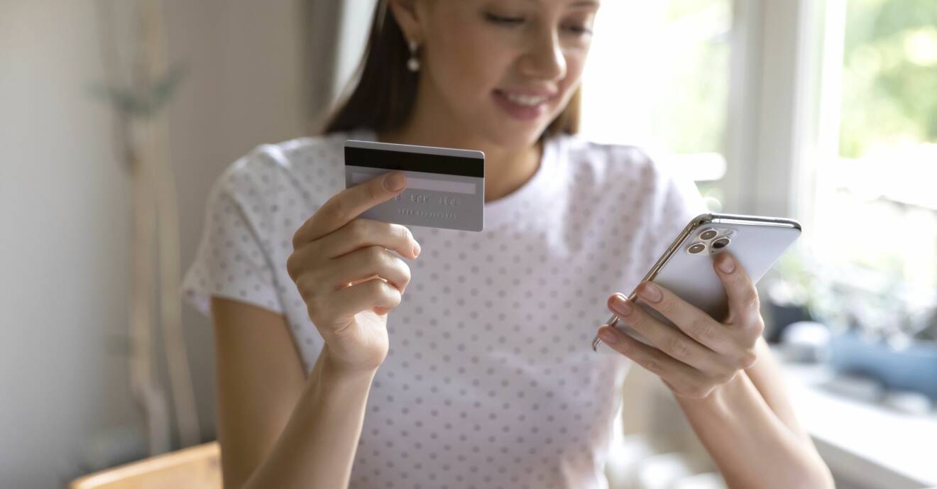 Ung kvinna sitter med ett bankkort och ska göra ett köp