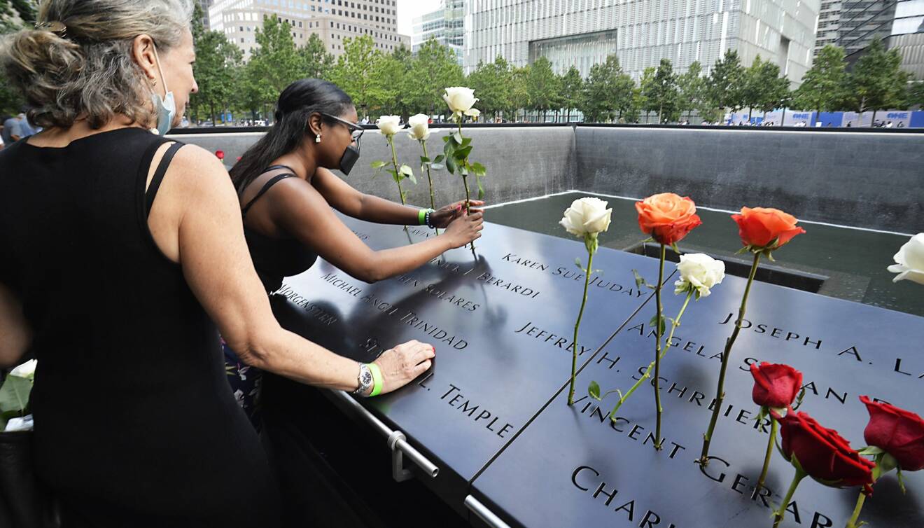 Två kvinnor med munskydd sätter blommor på minnesplatsen där de två tvillingtornen stod. m