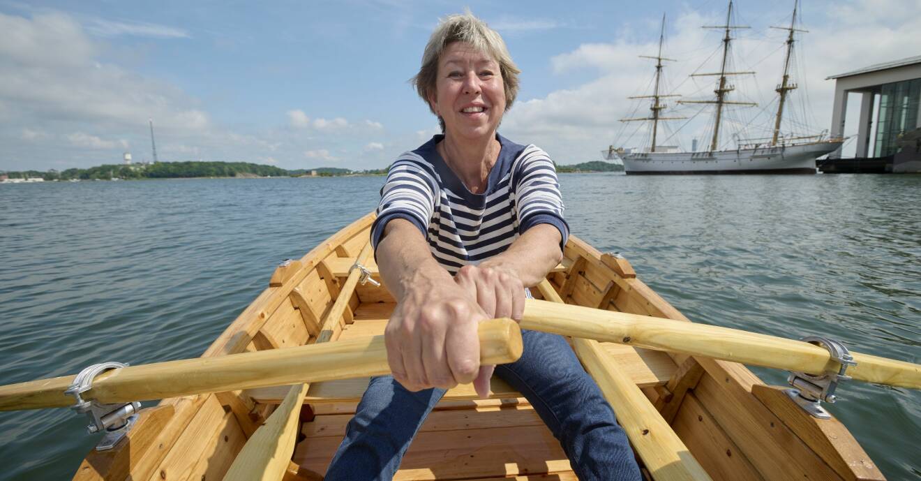 Eva Runesson sitter i båten som hon själv har byggt, ror ut från hamnen i Karlskrona och i bakgrunden syns Marinmuseum och öar i Karlskrona skärgård