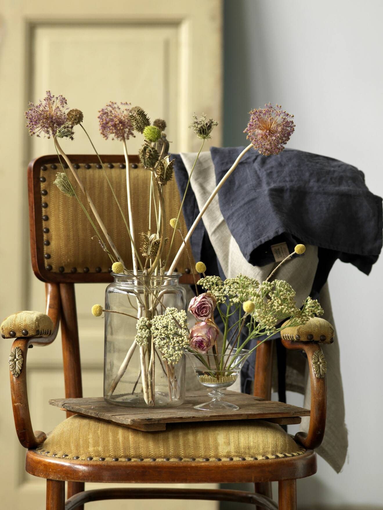 Två buketter torkade blommor i glasvaser på en stol.
