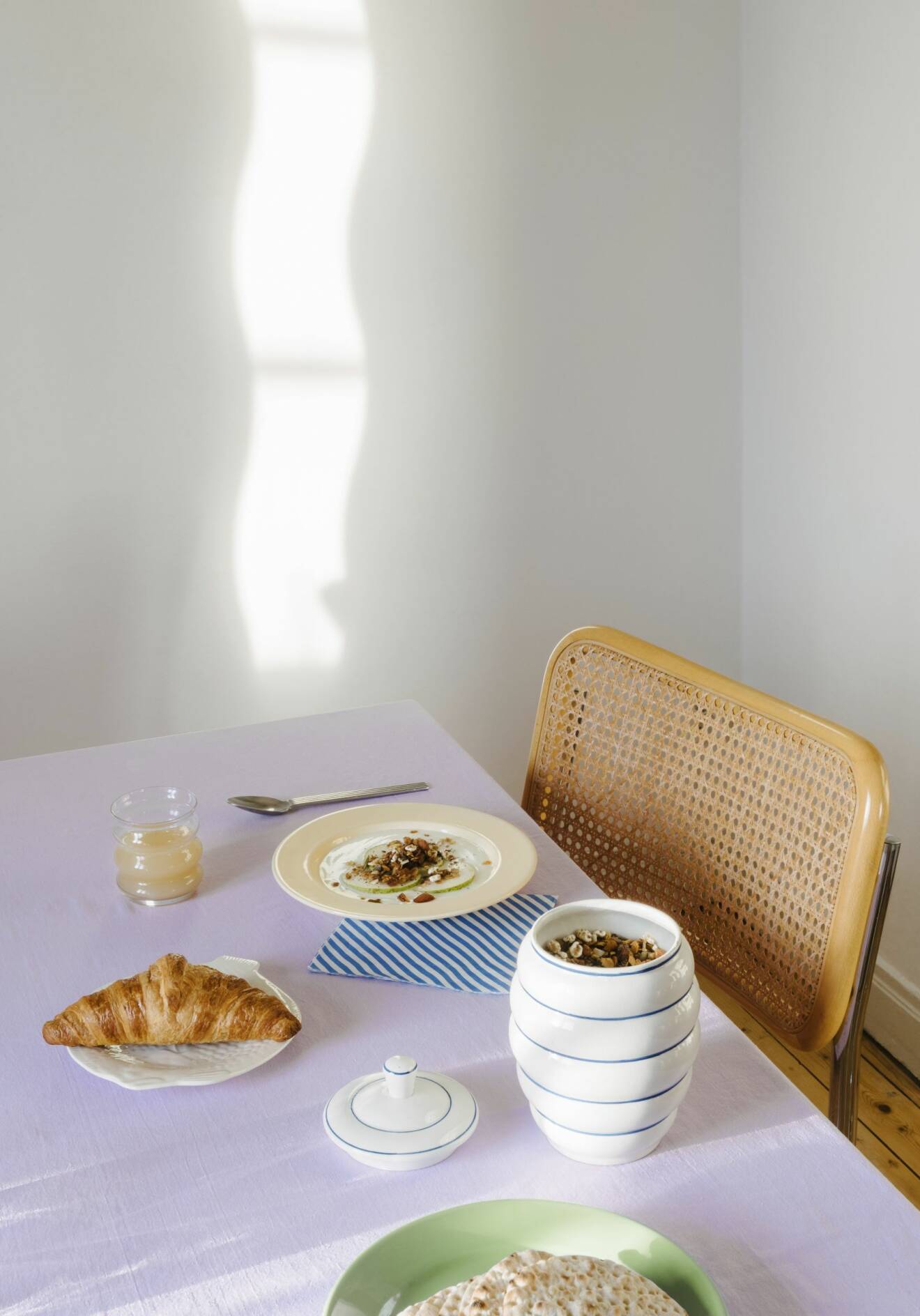 Frukost dukat på ett bord med lila duk, bredvid står en stol med rygg i korg.