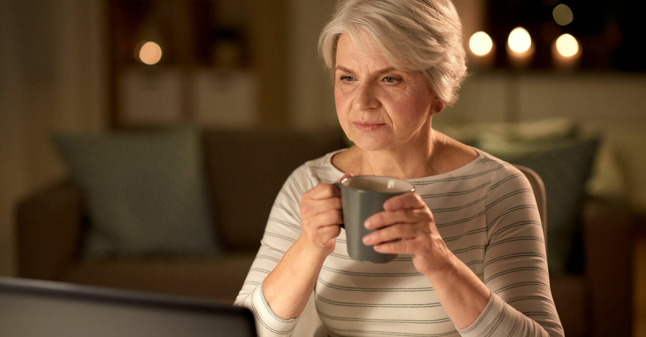 Kvinna sitter vid datorn och dricker kaffe.