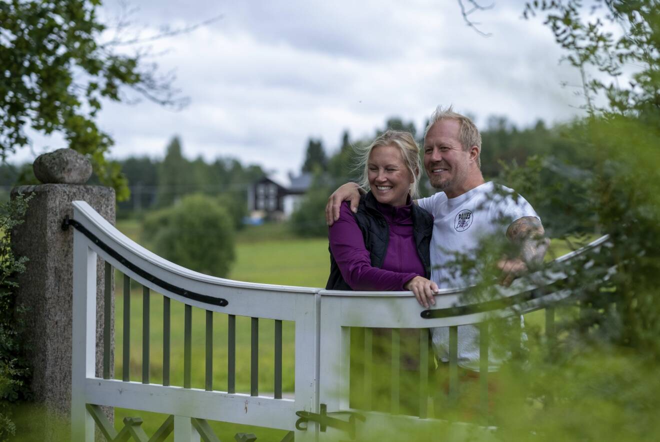 Karin Ås och Jon-Erik "Jeja" Andersson står och håller om varandra, lutade mot en grind i natursköna omgivningar.