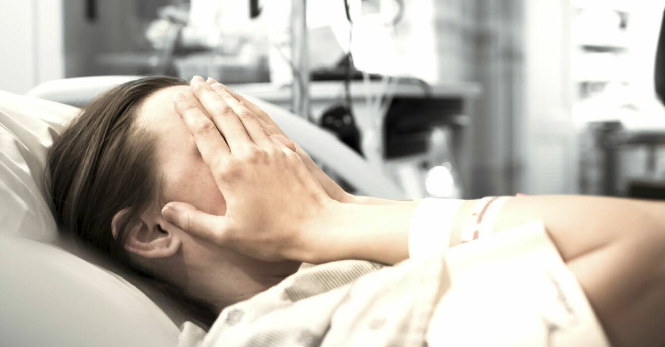 Ung kvinna ligger med händerna för ansiktet i en sjukhussäng