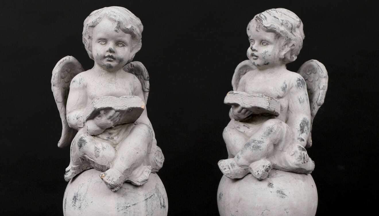 Två skulpturer i lergods, föreställnade två änglabarn som sitter på en sten med varsin bok i handen.