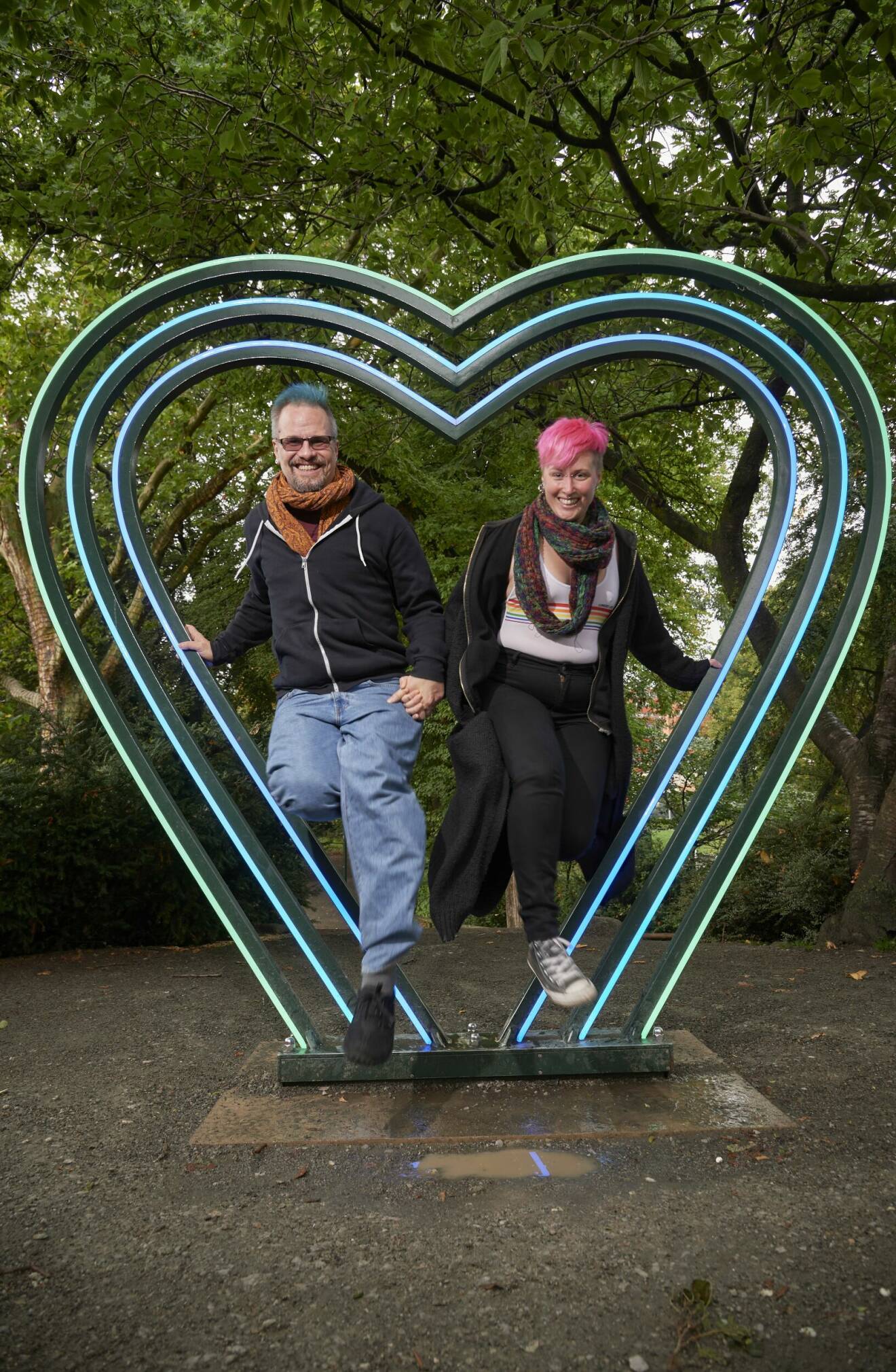 Patrik och Anna håller varandras händer när de hoppar igenom en stor hjärtskulptur.