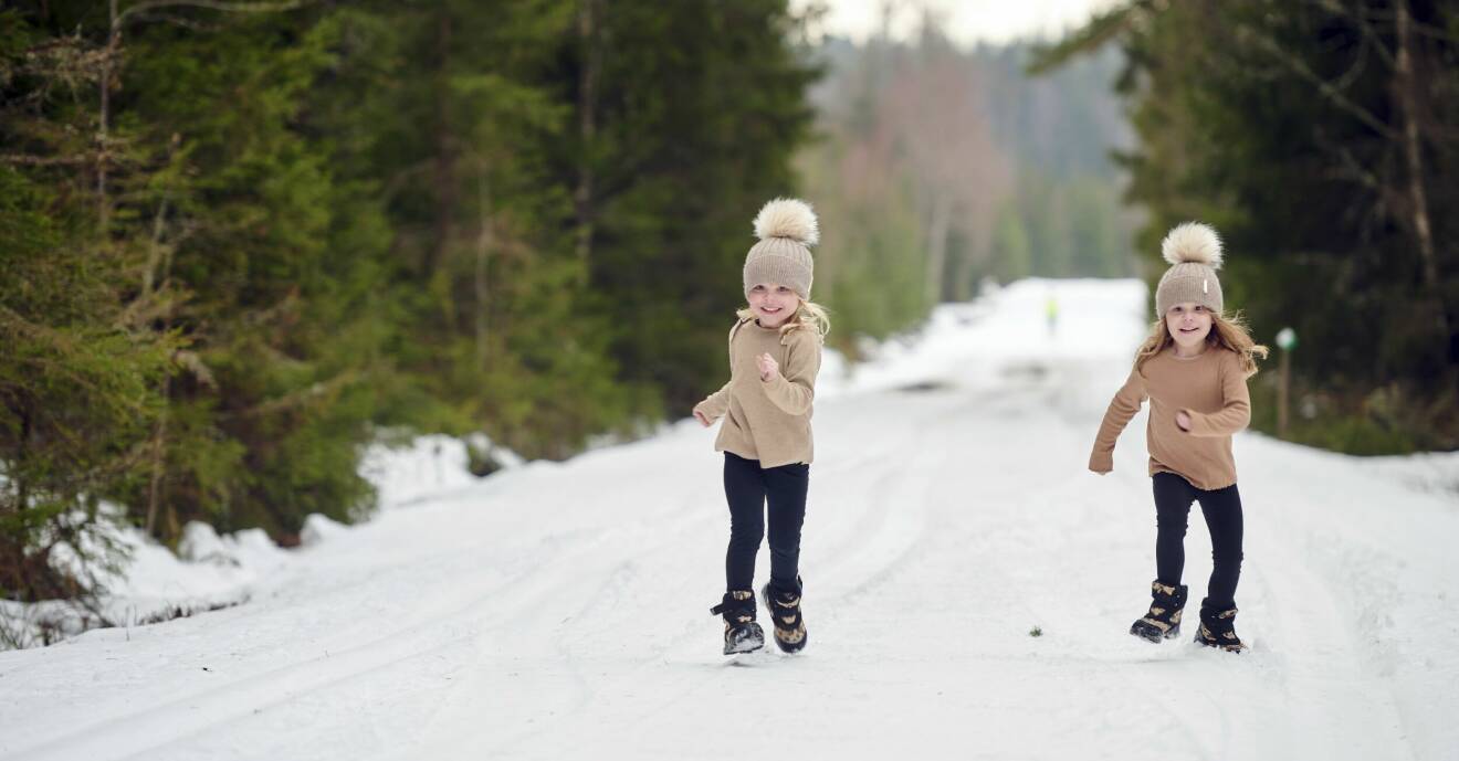Nomie och Minelle springer tillsammans i full fart på en snöig väg med granar på vardera sidan av vägen