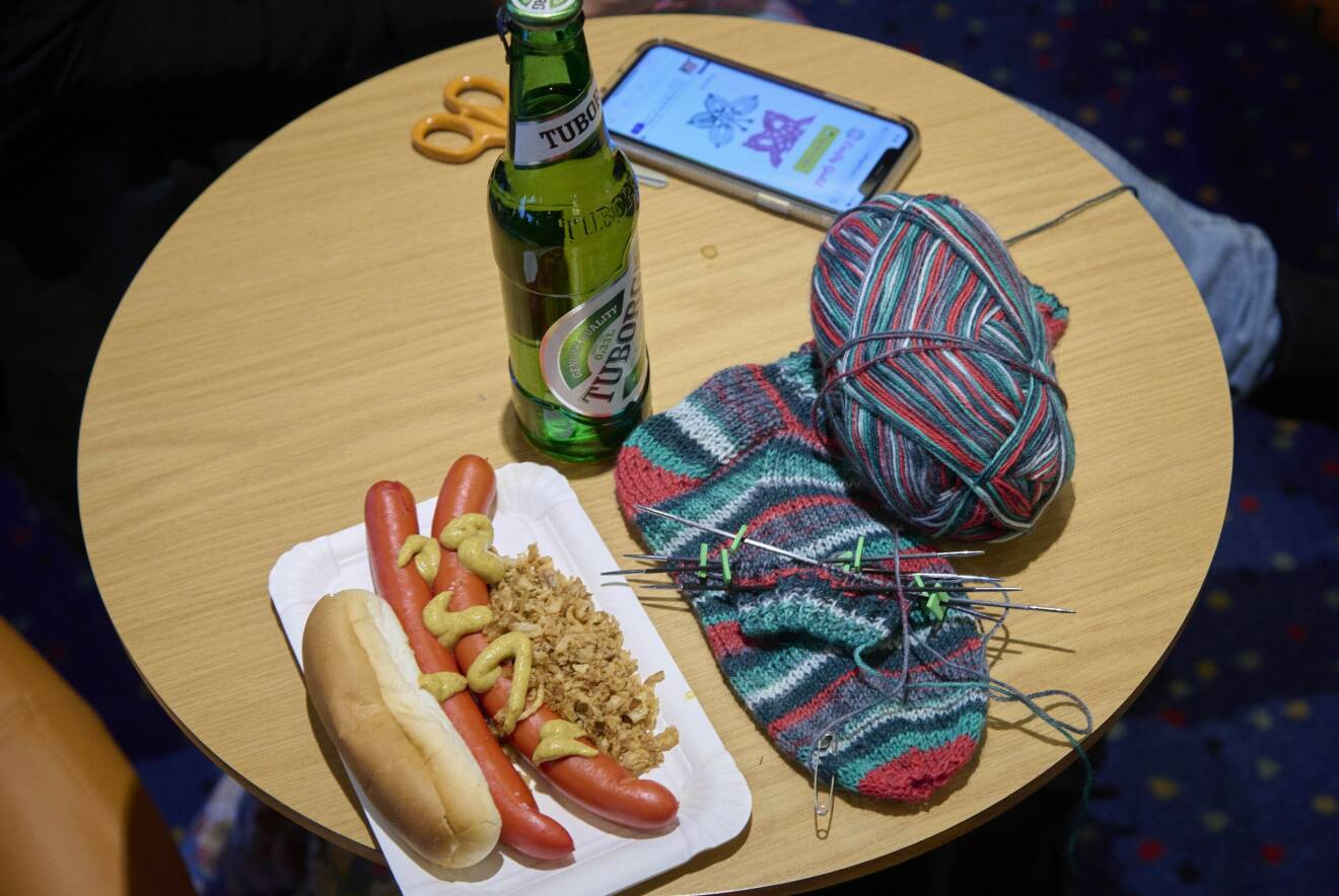 Öl, pölsor, färgglad strumpstickning, mobiltelefon och sax samsas om utrymmet på ett litet runt bord.
