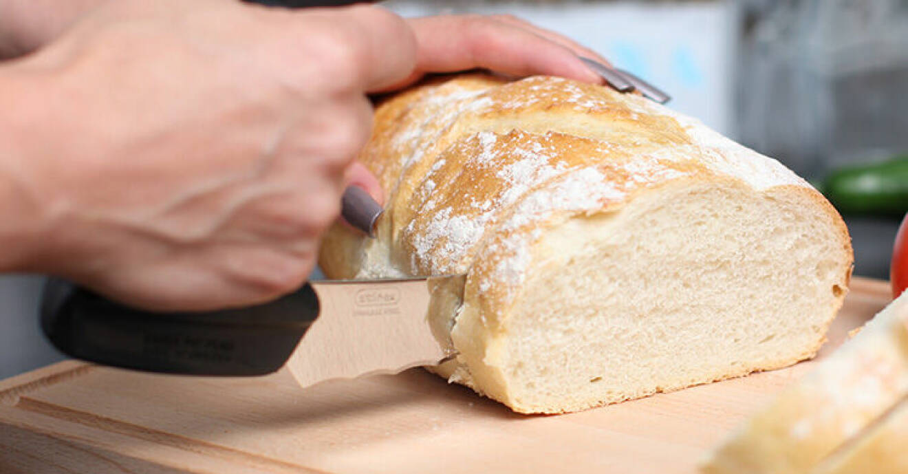 Ergonomisk brödkniv skär igenom en limpa vitt bröd.