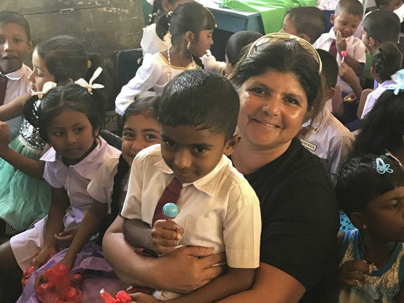 Yolanda har en pojke i knät där hon sitter med en massa barn på en skola i Sri Lanka.