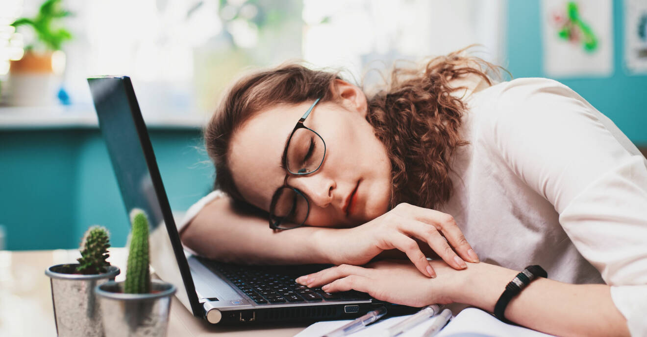 Kvinna med lockigt hår och glasögon har somnat vid sin laptop