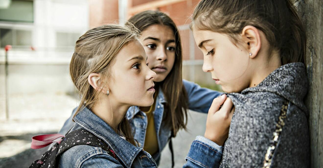 En ung flicka trycker upp en annan flicka mot en vägg utomhus.