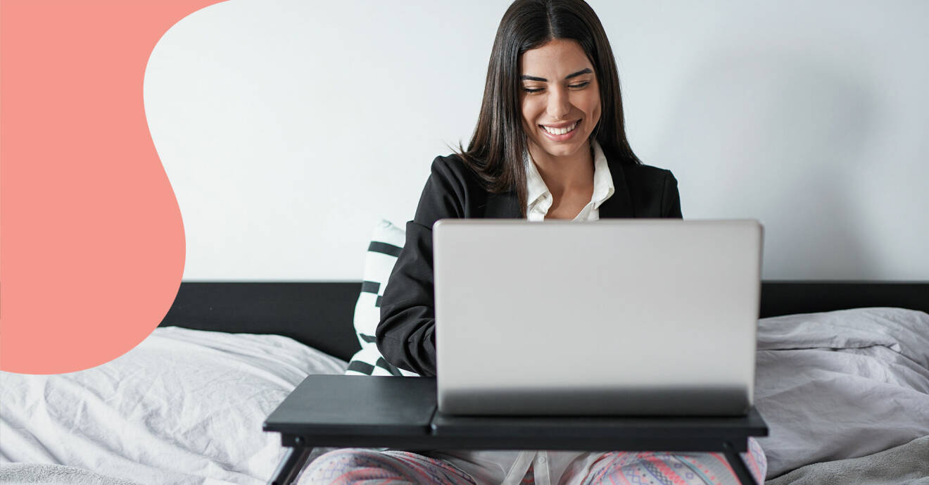 Kvinna jobbar med datorn i pyjamas i sängen.