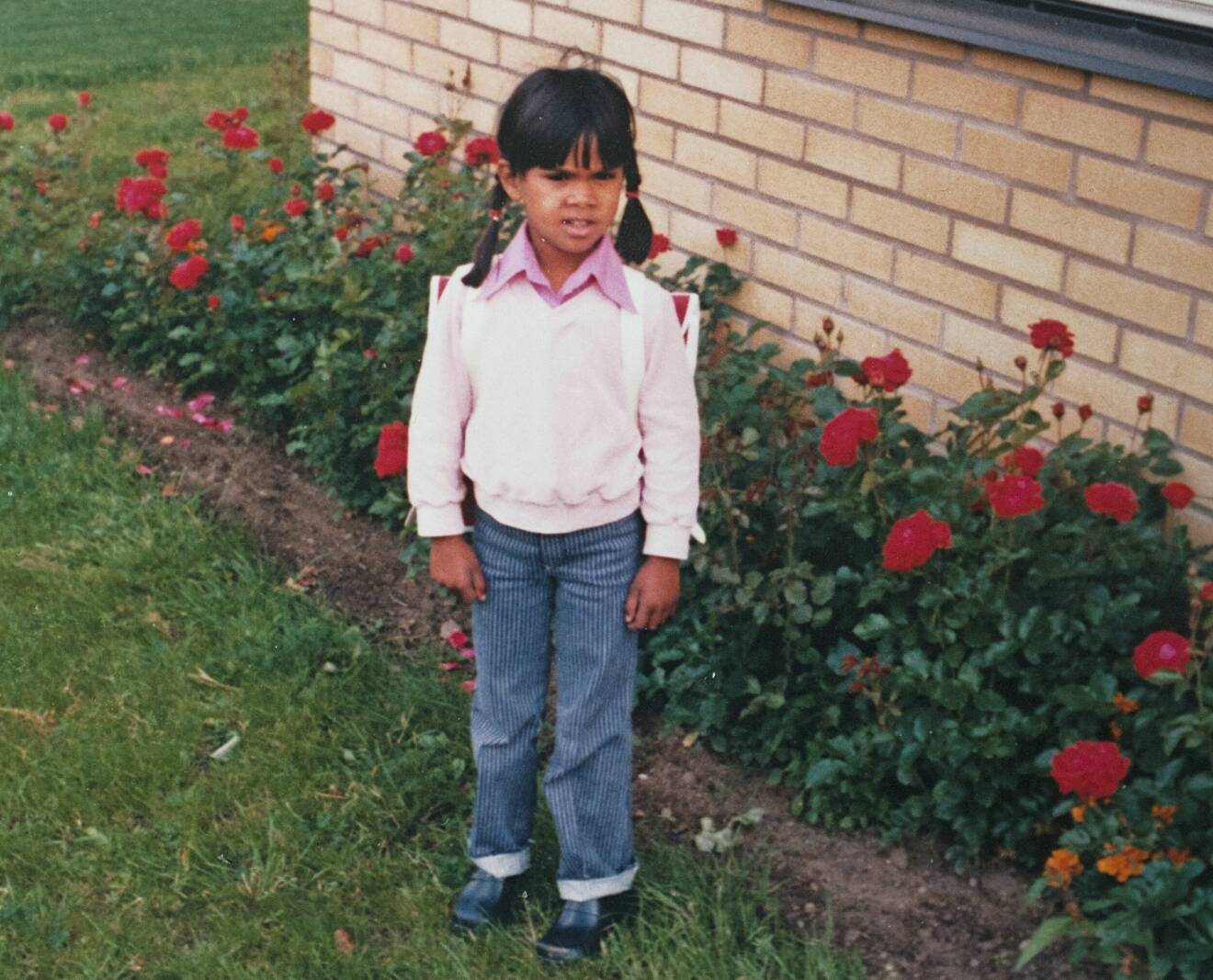 Meénakshi kom till Sverige som adoptivbarn när hon var 2,5 år och hon står i trädgården framför rosenrabatten intill villan