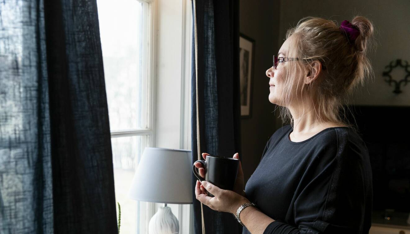Johanna Brinck står med en kopp kaffe intill sitt fönster i villan i Vingåker.