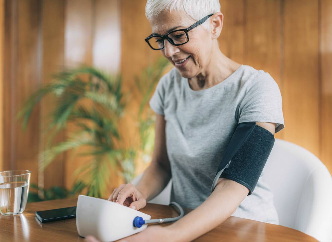 Kvinna sitter vid ett bord och mäter själv sitt blodtryck.