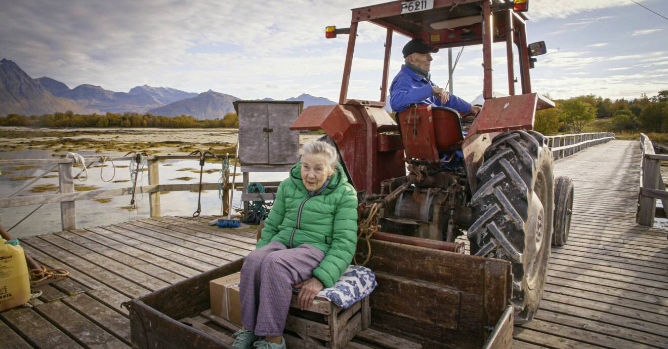 En man kör en traktor och en kvinna åker med på ett släp.