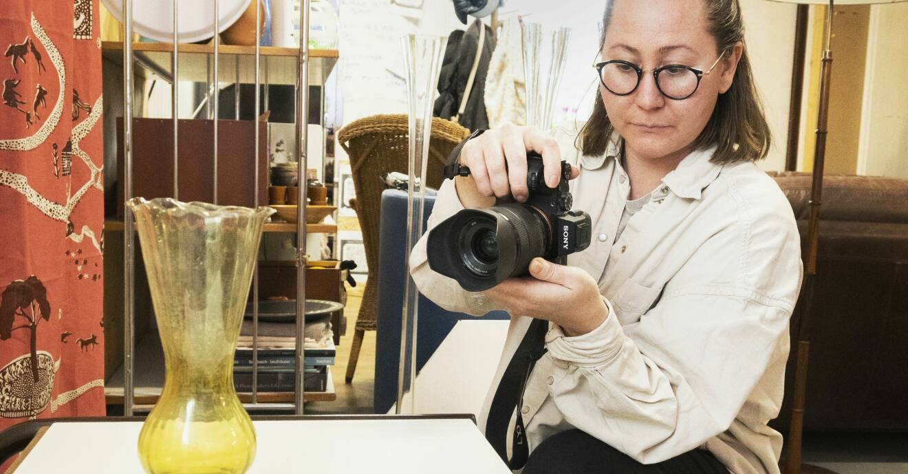 Amanda fotograferar en vas som står på ett bord och i bakgrunden syns möbler och föremål.