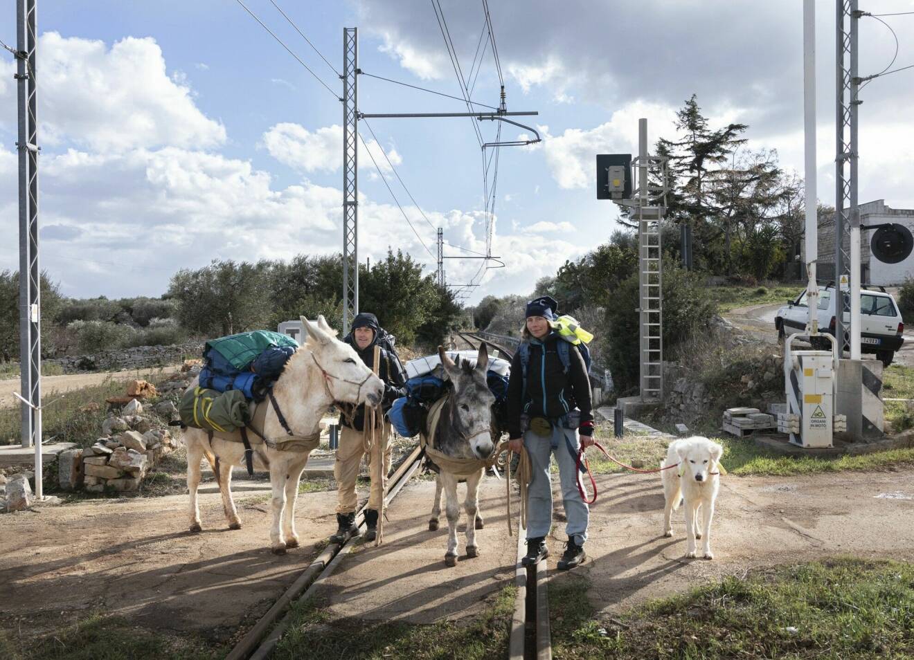 Helena Kågemark, Carlo Magnani, deras två åsnor och hund står på en järnvägsöverfart i vandringsutrustning.