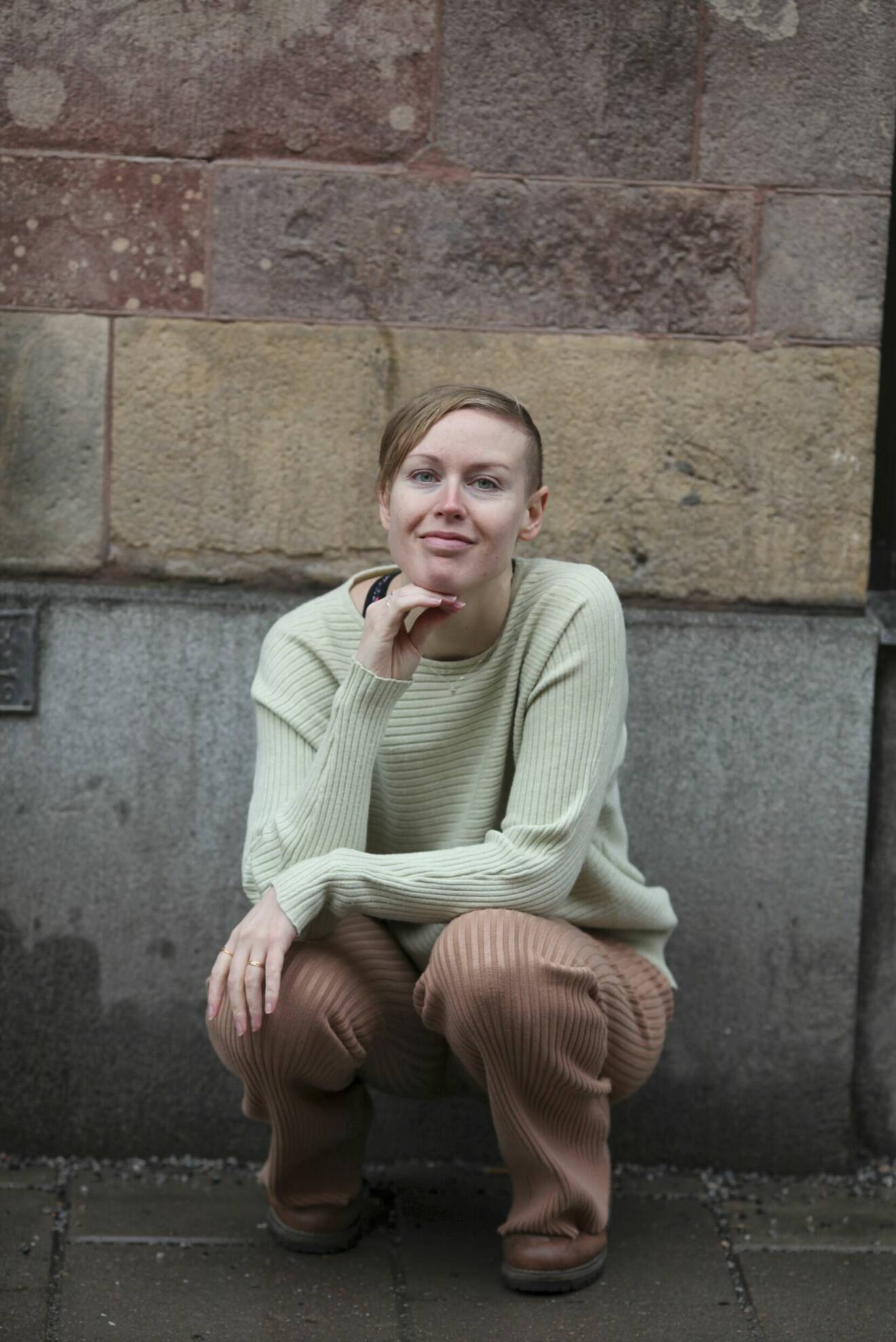 Erika Lindquist sitter på huk framför en tegelvägg.