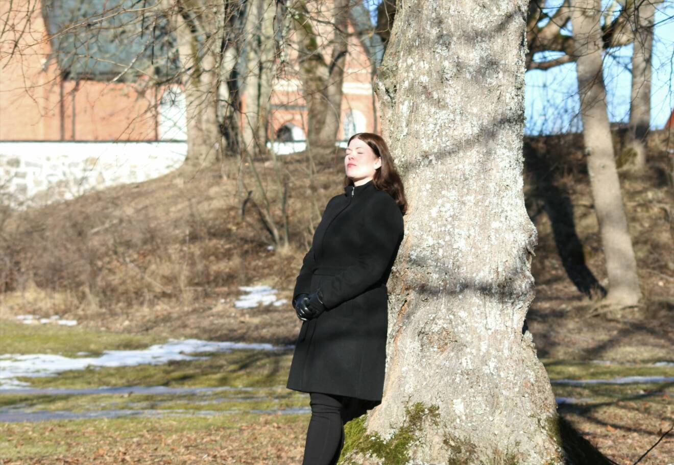 Jenny Wernborg i Västerås står lutad mot ett träd och njuter av solen med stängda ögon.