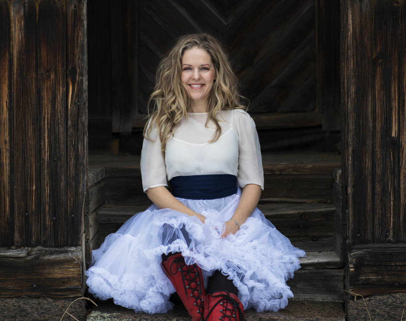 Artisten Sofia Karlsson ler, sitter på en stentrappa.