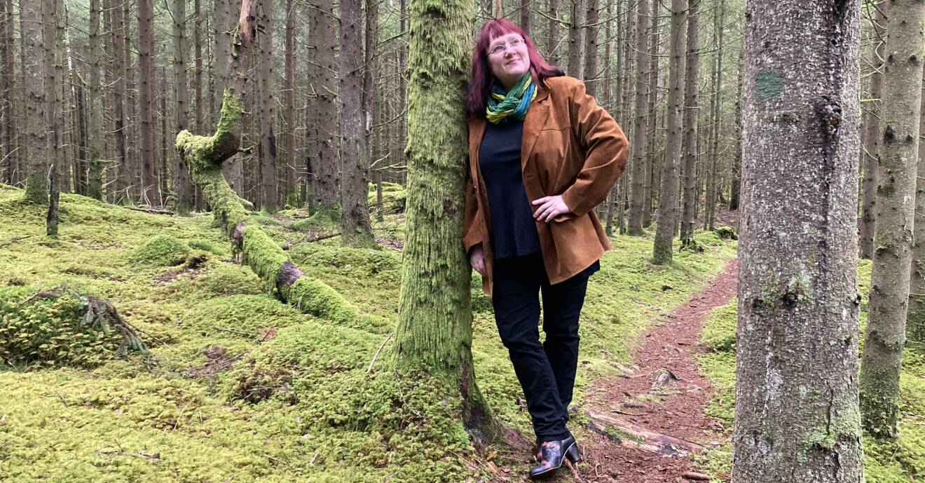 Ingela Wadbring, professor och författare, står lutad mot ett träd i skogen.