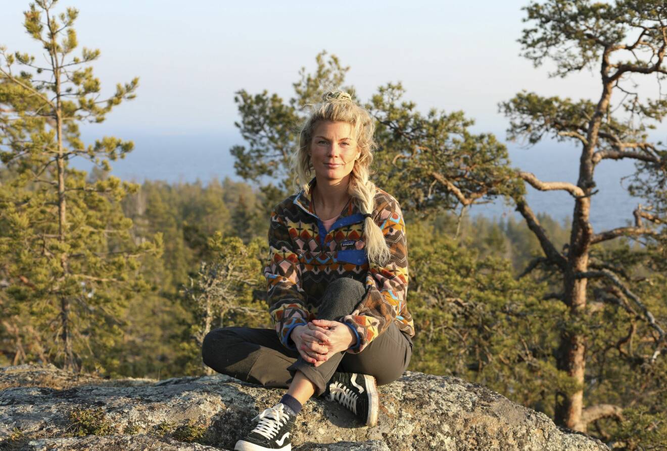 En ung kvinna sitter på Krokviksberget i Sundsvall med tallar och hav i bakgrunden.