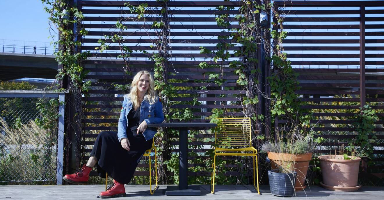 Författaren Sofie Weidemann sitter i jeansjacka på en terass med krukor och spaljé, ler.