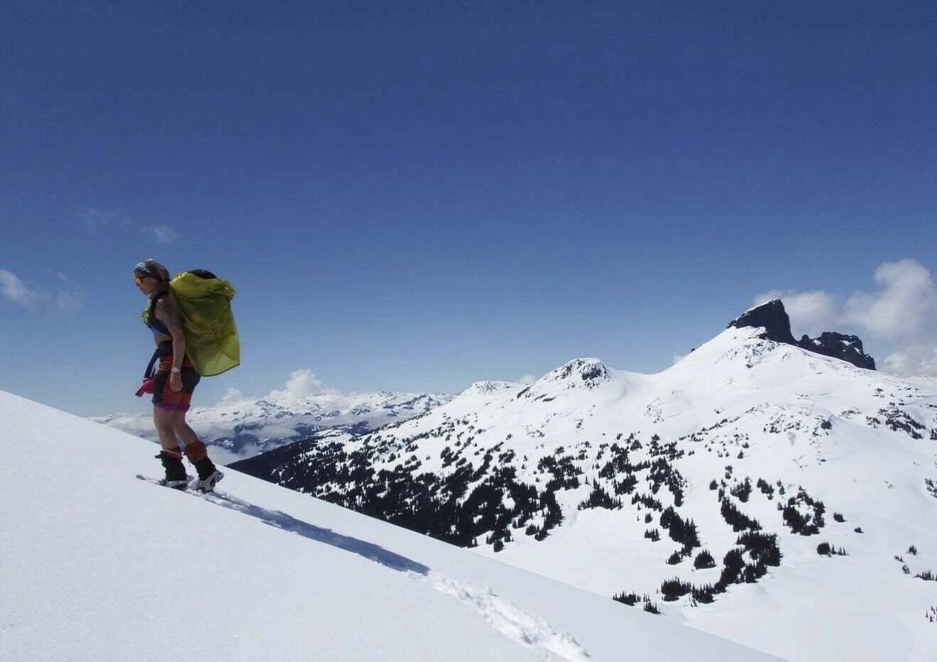 En ung kvinna vandrar uppför ett snötäckt berg, med stor ryggsäck på ryggen.
