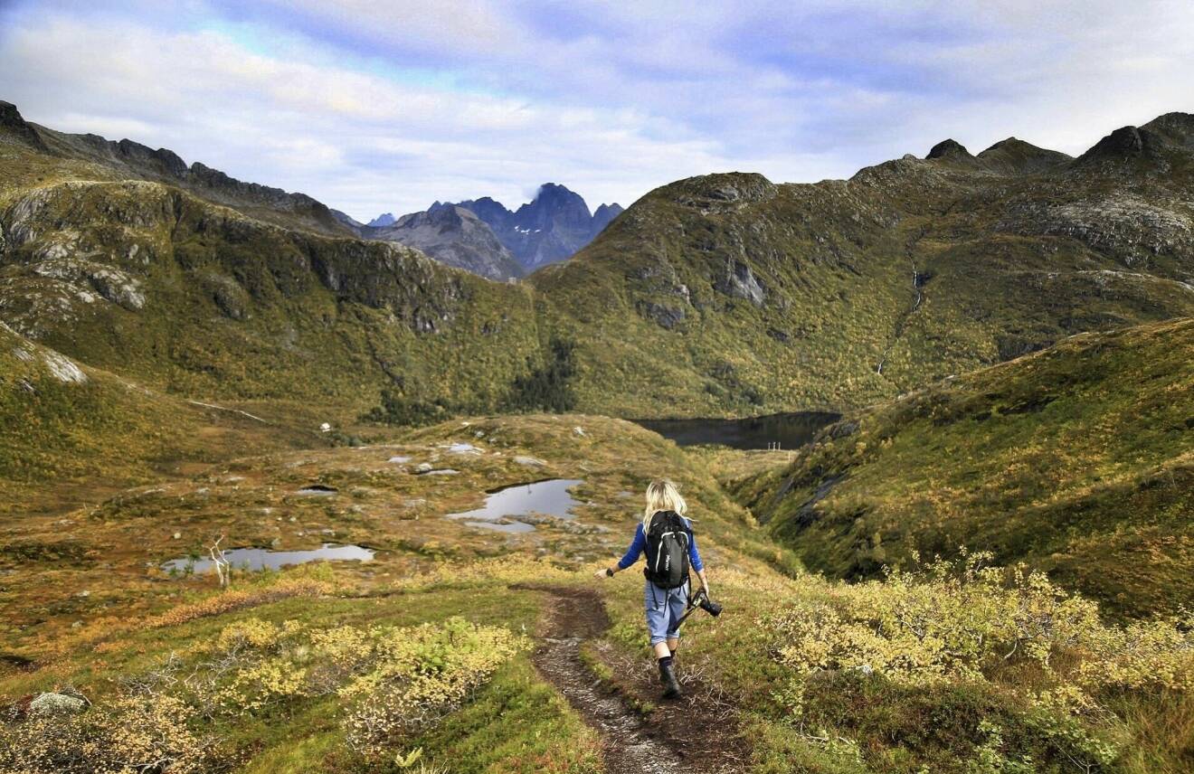 En ung kvinna går på ett grönt fjäll med berg i fjärran.