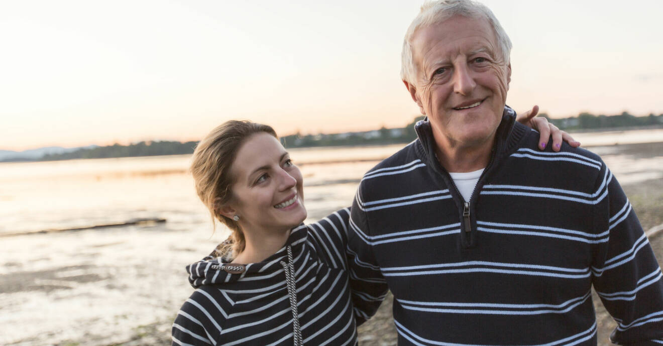 En man i 60-årsåldern och hans vuxna dotter promenerar på stranden.