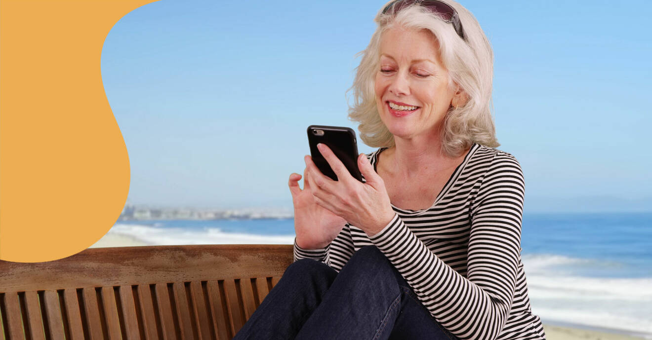 Bilden visar en kvinna på stranden som använder mobilen.