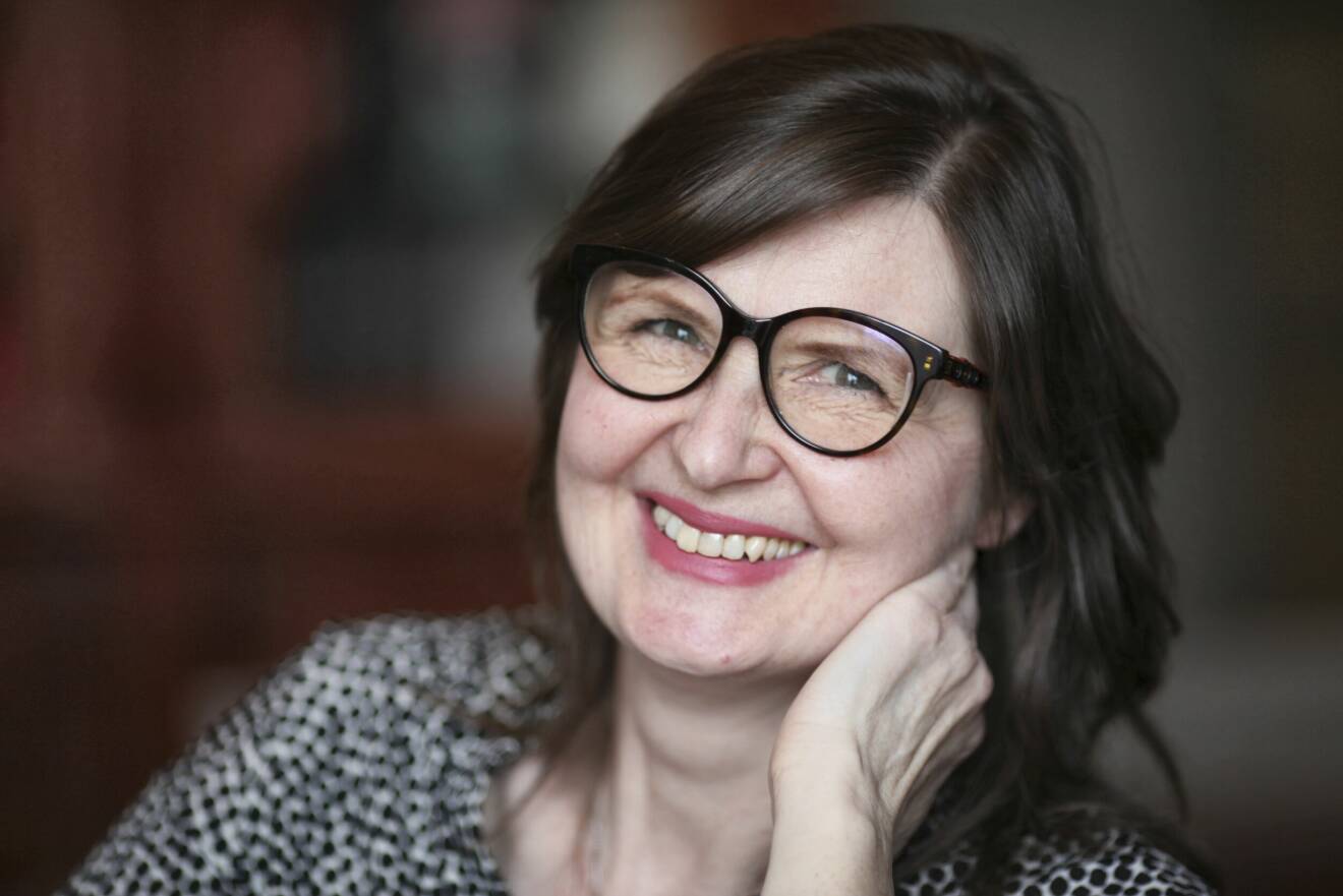 Författaren Nina van den Brink, leende i glasögon och rosa läppstift.
