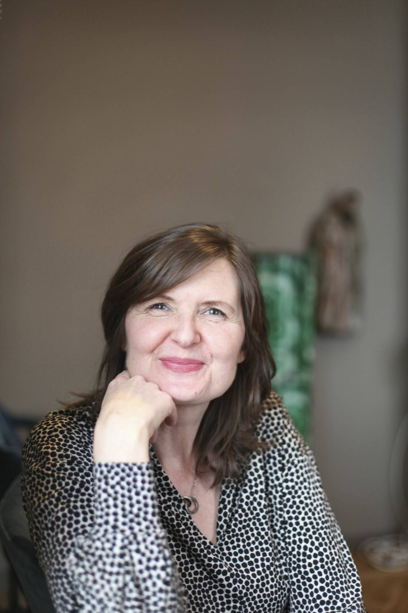 Författaren Nina van den Brink, lutar huvudet mot handen och ler in i kameran.