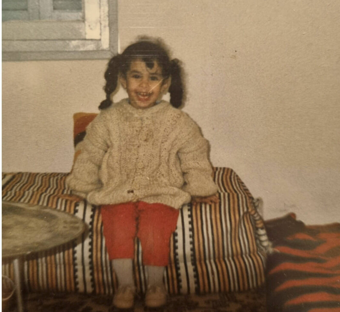 En bild från barndomen i Algeriet där Fatma sitter på en bädd med randigt överkast