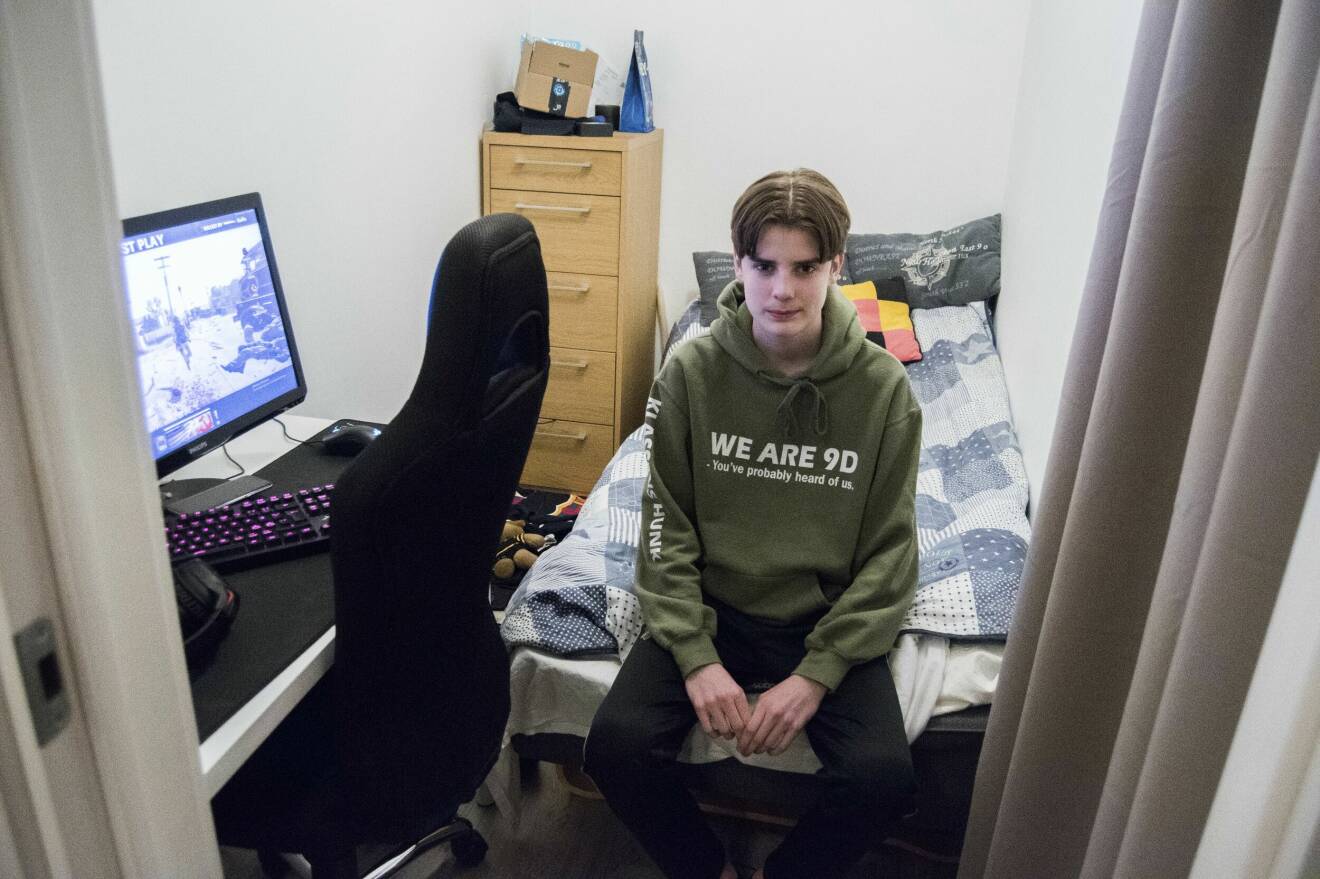 En tonårsson i ett litet rum med dator och skrivbordsstol.