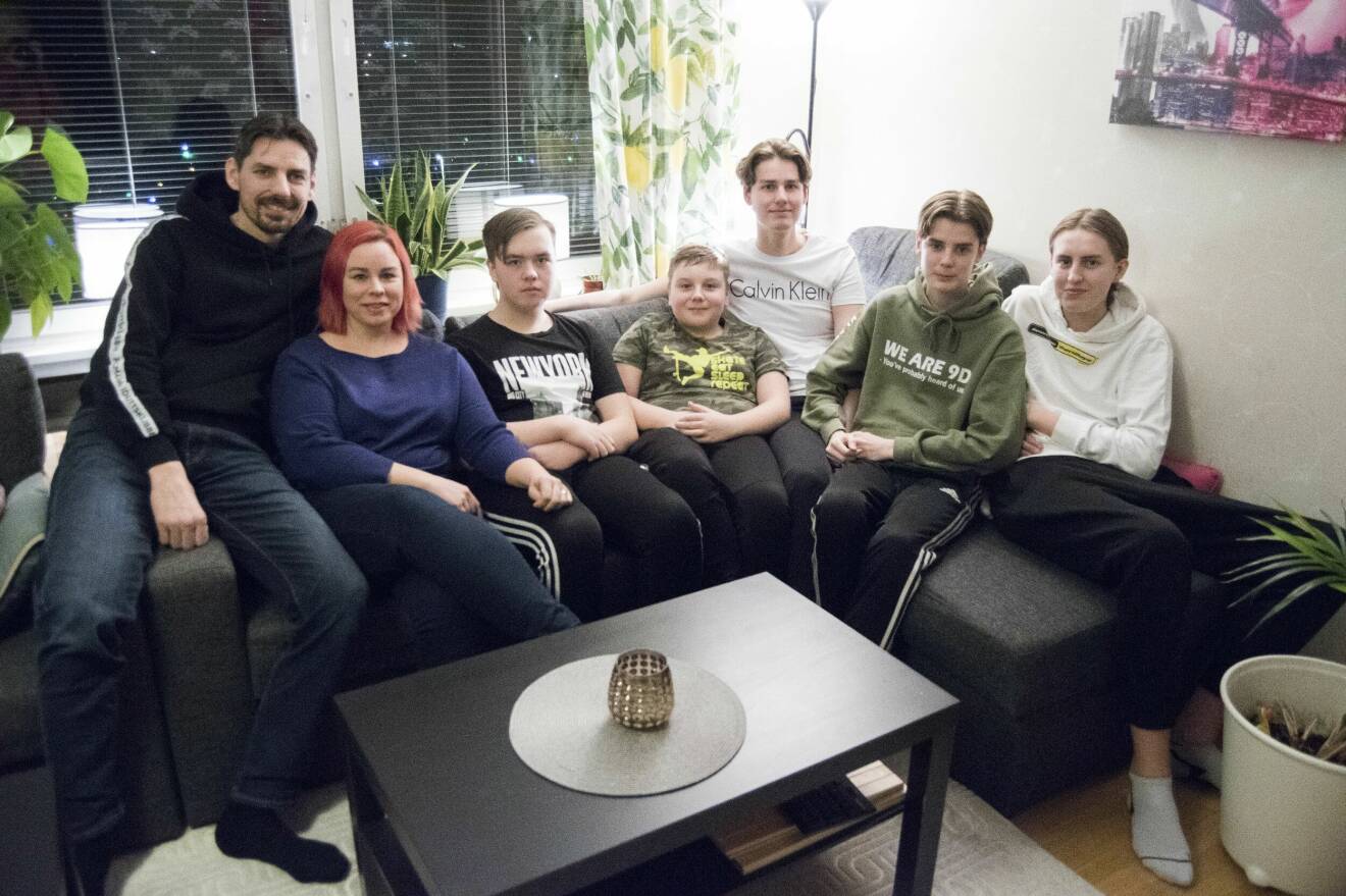 En stor bonusfamilj med två vuxna och fem barn sitter i en soffa.
