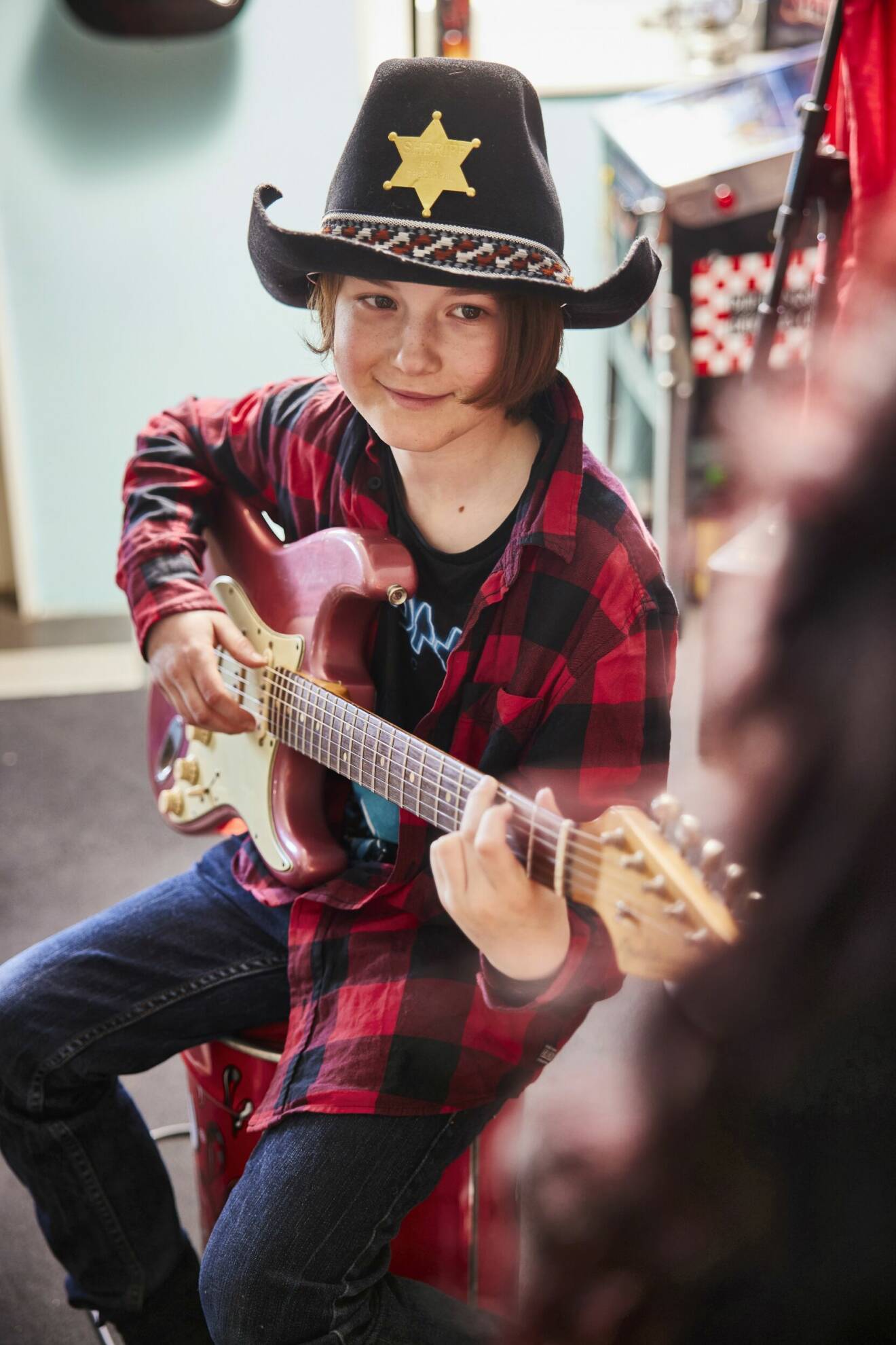 En ung pojke med cowboyhatt spelar på en elgitarr.