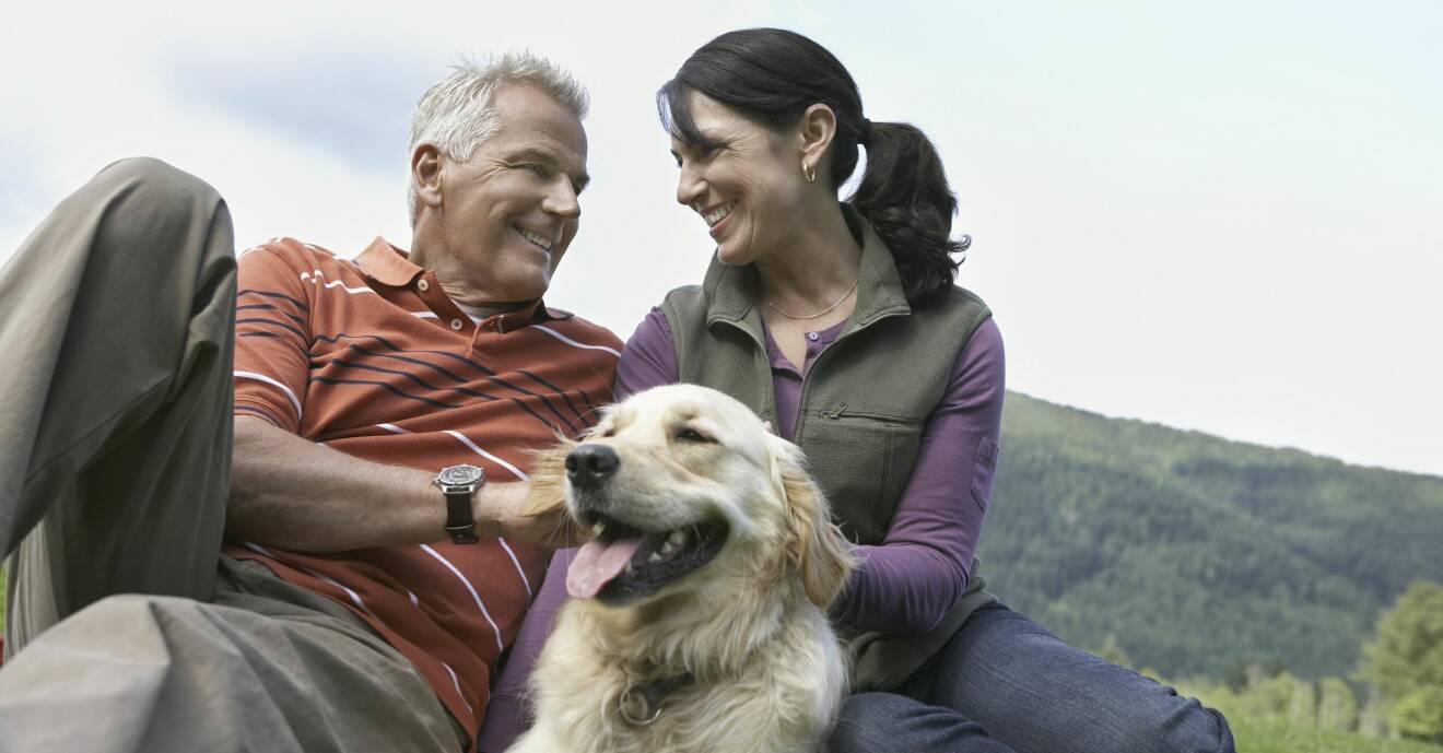 Ett medelålders par sitter ute i naturen och tittar förälskat på varandra. Mellan sig har de en hund.