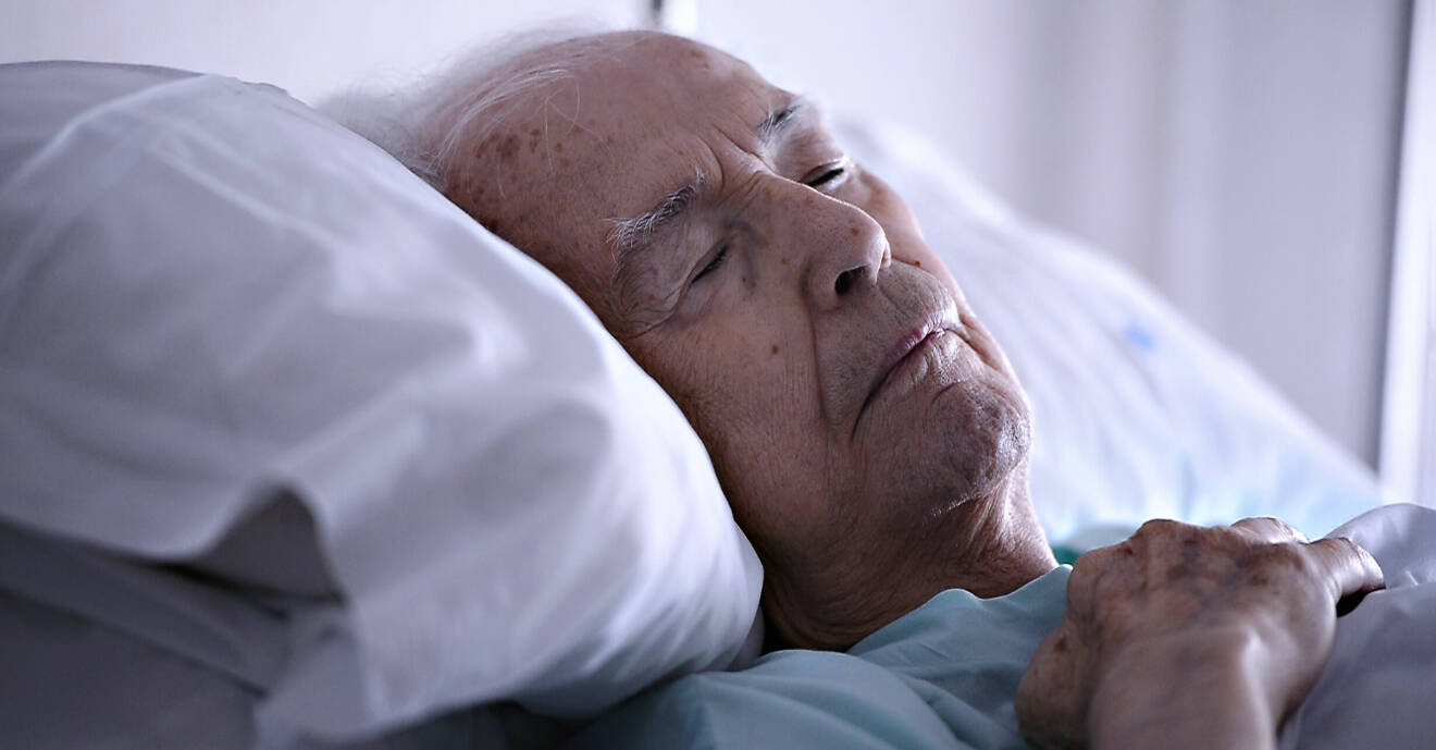 En gammal man ligger med slutna ögon i en sjuksäng.