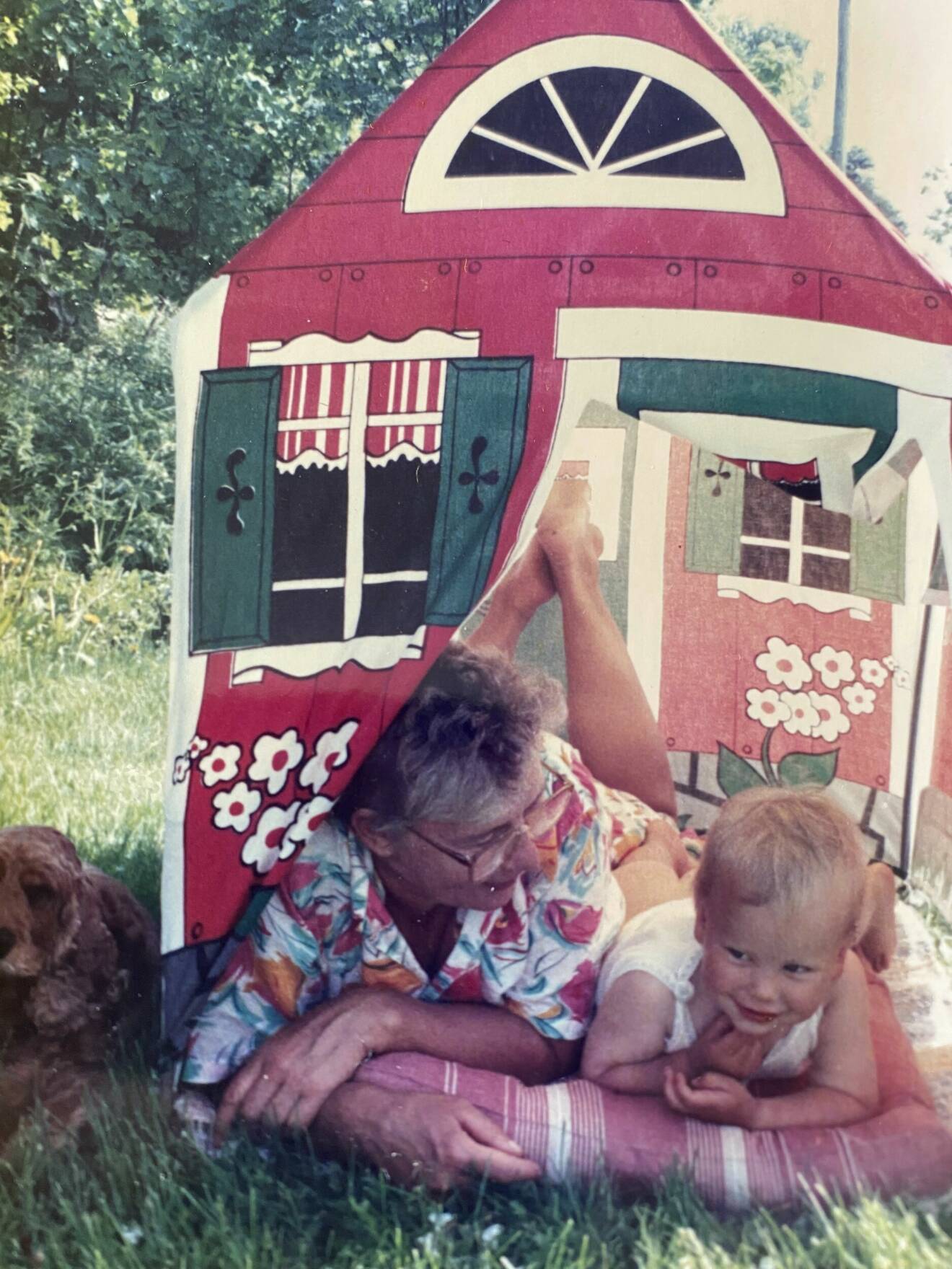 Skådespelaren Amanda Jansson som barn med sin mormor Barbro i ett leksakstält på en gräsmatta.
