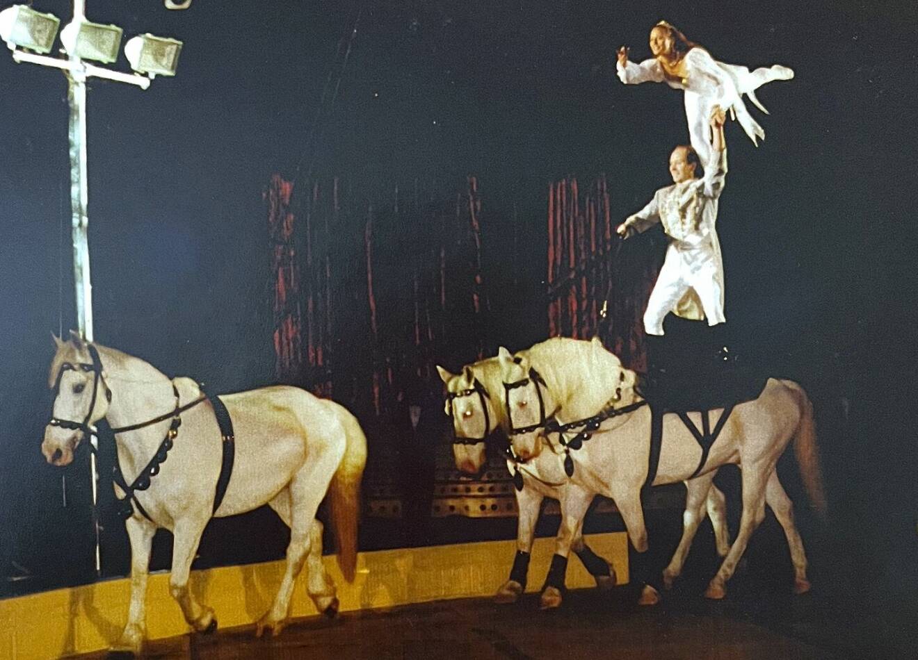 Carlos och Susanne gör ett nummer i cirkusmanegen där han står med varsitt ben på två hästar och hon står med ena benet på hans axel, sträcker ut det andra håller Carlos i en hand.