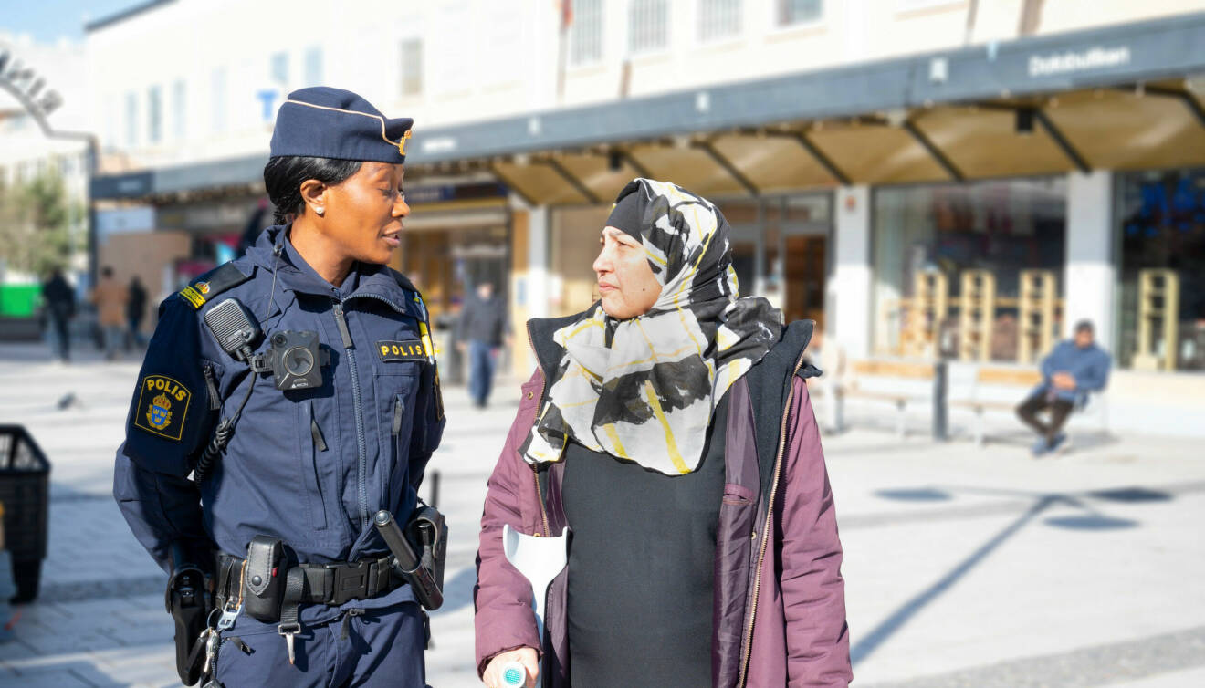 Polis pratar med kvinna på ett torg.
