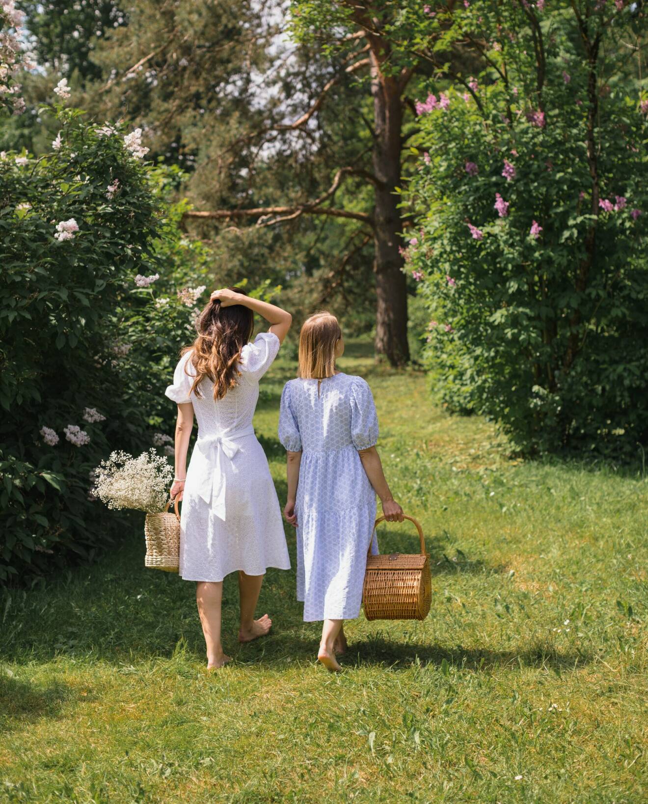 Två kvinnor går barfota i gräset med picknickkorg i handen.