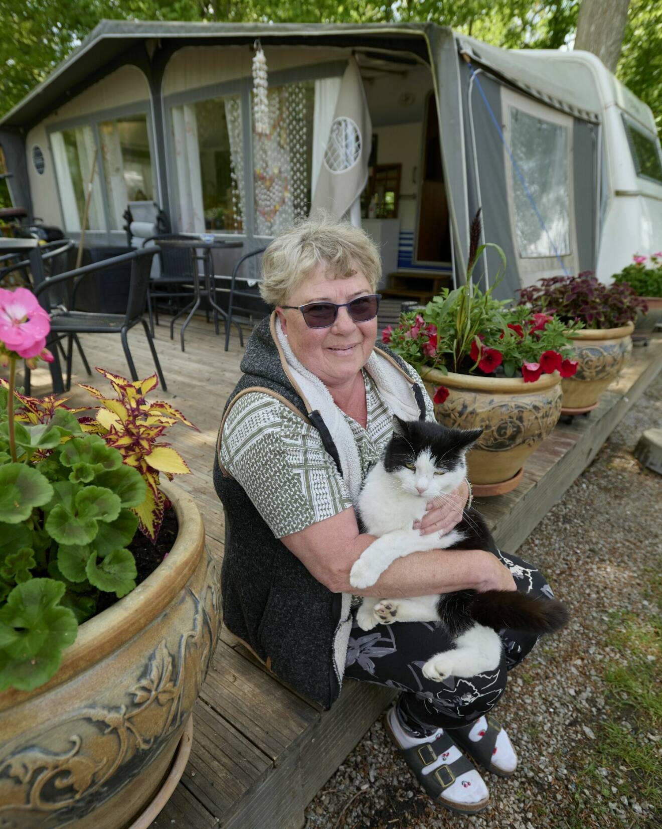 Liselott sitter på trädäcket utanför sin husvagn mellan två stora krukor med blommor och håller katten Ponglan i knät som flyttade in till henne för nio år sedan.