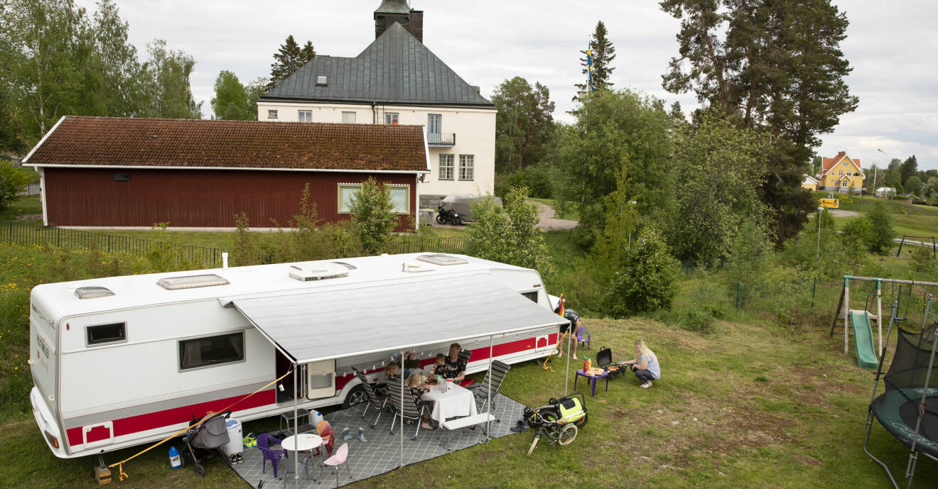 Drönarbild på familjen Fridland-Engströms stora husvagn som står parkerad på familjens tomt. Utanför husvagnen grillar Linda korv och Erik sitter med barnen runt middagsbordet.